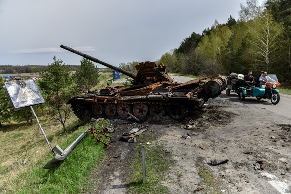 epa09908824 People ride a motorcycle on a road near destroyed Russian tank in recaptured by the Ukrainian army Rusaniv village of Kyiv area, Ukraine, 25 April 2022. Russian troops entered Ukraine on 2 ...