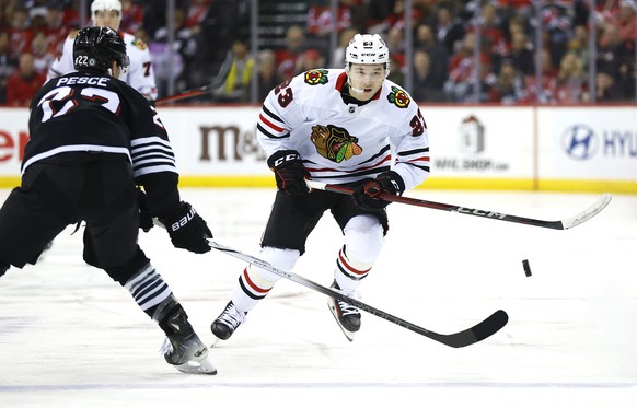 Chicago Blackhawks center Philipp Kurashev (23) plays the puck past New Jersey Devils defenseman Brett Pesce (22) during the first period of an NHL hockey game, Saturday, Dec. 14, 2024, in Newark, N.J ...