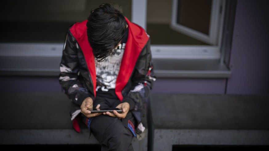 Ein Mann sitzt auf einer Bank und benutzt sein Mobiletelefon, aufgenommen waehrend eines Medienrundgans im Bundesasylzentrum Zuerich, am Donnerstag, 27. Oktober 2022 in Zuerich. (KEYSTONE/Michael Buho ...
