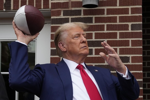 Former President Donald Trump prepares to throw a football to the crowd during a visit to Alpha Gamma Rho, an agricultural fraternity, at Iowa State University before the start of an NCAA college football game.