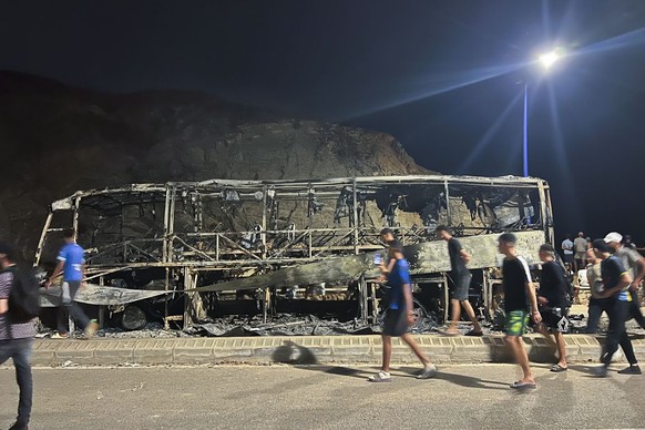 epa13143319 Young Moroccans walk past a burned-out bus following unrest on the road leading to the Castillejos border crossing with Ceuta in Castillejos, Morocco, 31 July 2026. Spain and Morocco agree ...