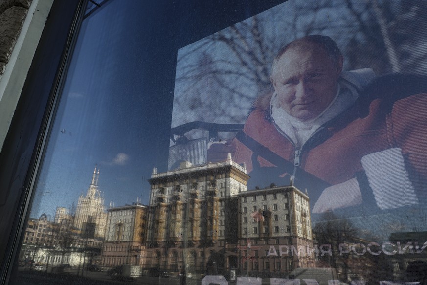 epaselect epa09791394 The US Embassy is reflected in a store window showing a photo of Russian President Vladimir Putin, in Moscow, Russia, 28 February 2022. The embassy urged US citizens to leave Rus ...