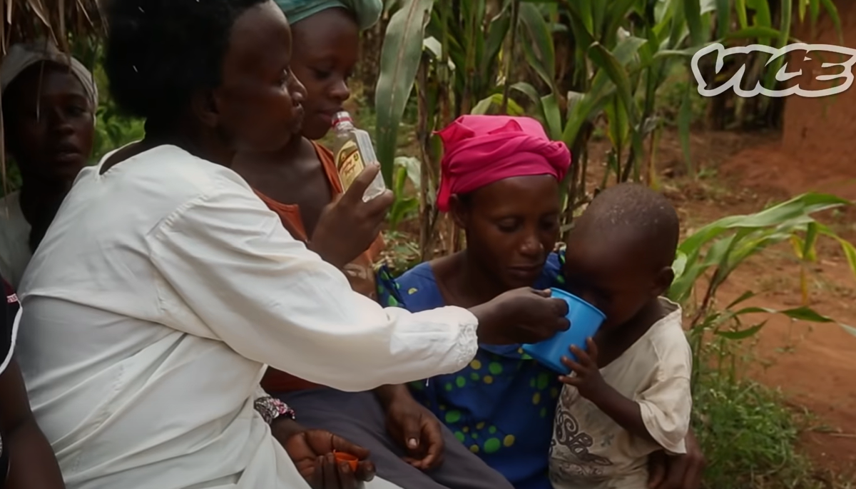 Frauen geben einem Kleinking in Uganda "Waregi", selbstgebrannter Alkohol, zum Trinken.