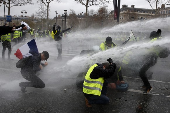 epaselect epa07202670 Protesters wearing yellow vests (gilets jaunes) are sprayed with water cannons as they clash with riot police near the Arc de Triomphe during a demonstration over high fuel price ...