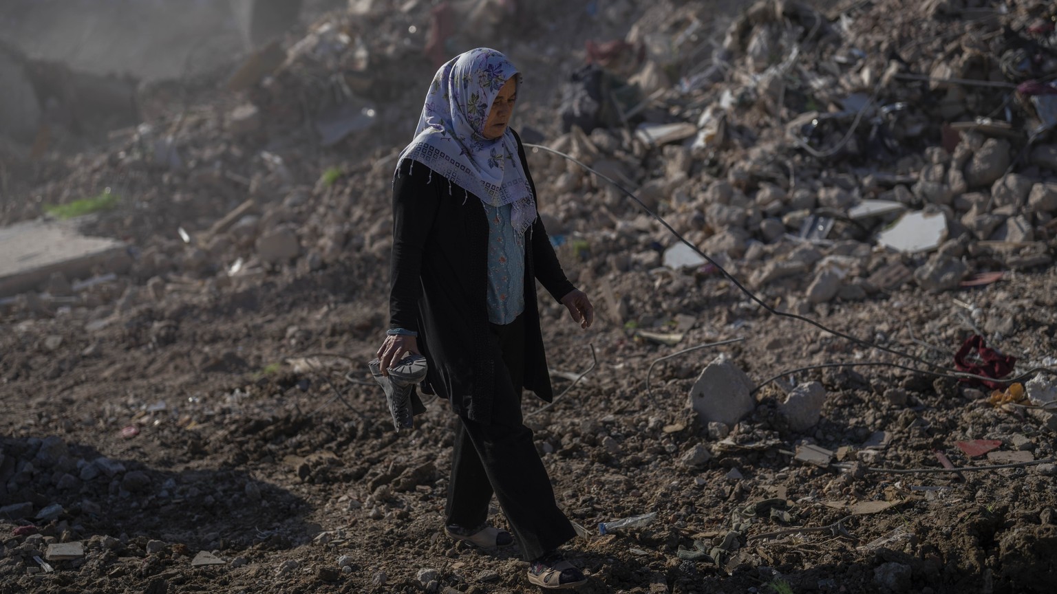 A woman that lost a family member holds a boot as she walks out of the debris of a compound destroyed during the earthquake in Antakya, southeastern Turkey, Tuesday, Feb. 14, 2023. The death toll from ...