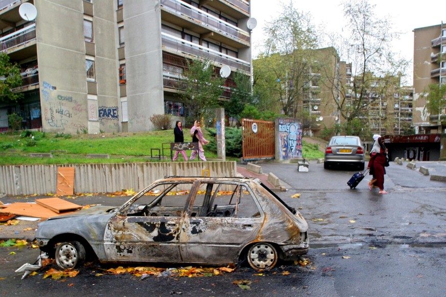 Clichy-sous-Bois residents walk past the wreckage of a burnt car, Wednesday, Nov. 2, 2005, east of Paris. French President Jacques Chirac called for calm and a firm hand Wednesday in response to six n ...