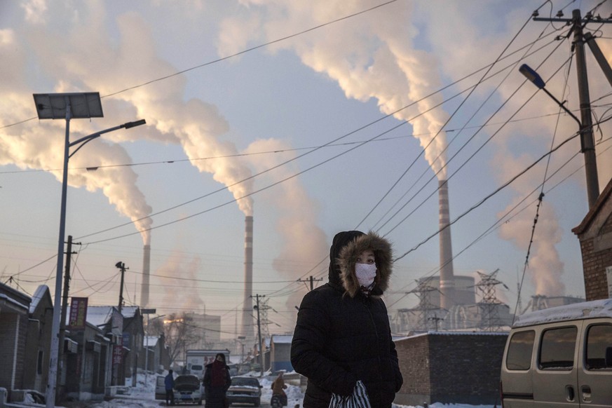 SHANXI, CHINA -NOVEMBER 26: (CHINA, HONG KONG, MACAU, TAIWAN OUT) Smoke billows from stacks as a Chinese woman wears as mask while walking in a neighborhood next to a coal fired power plant on Novembe ...