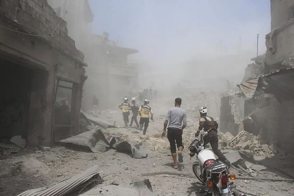 This photo provided by the Syrian Civil Defense group known as the White Helmets, shows Civil Defense workers running in a street that was hit by Syrian government airstrikes, in Jisr al-Shughur, sout ...