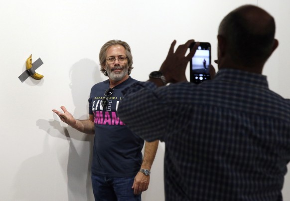 epa08047505 Art patrons take a picture with Italian artist Maurizio Cattelan piece's 'Comedian' (a banana duct taped to the wall) during Art Basel in Miami, Florida, USA, 05 December 20 ...