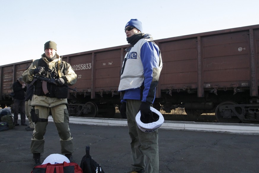 OSZE-Beobachter (rechts) &nbsp;neben einem Soldaten in der Nähe von Donetzk. Im Hintergrund abfahrbereite Zugwaggons mit den Wrackteilen des abgeschossenen Flugs MH17.