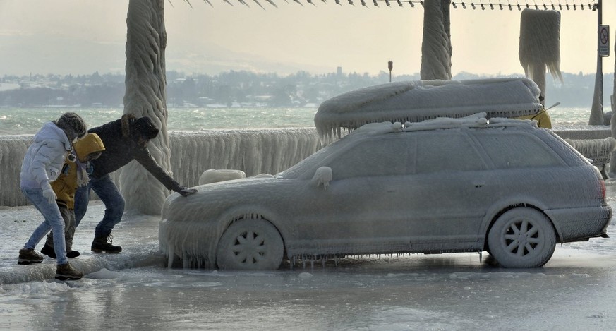 Des personnes se tiennent a une voiture recouvert de glace, une bise tempetueuse a cree de somptueuses sculptures de glace au bord du lac Leman dans la region de Versoix pres de Geneve, ce samedi 4 fe ...