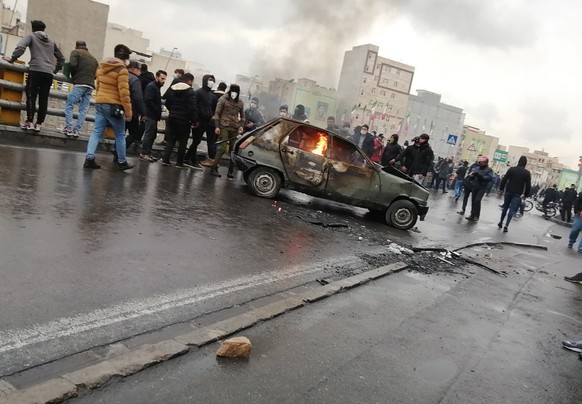 epa08002045 Iranian protesters stand around a vehicle set ablaze during clashes following fuel price increase in Tehran, Iran, 16 November 2019. Media reported that people protested on highways a day  ...