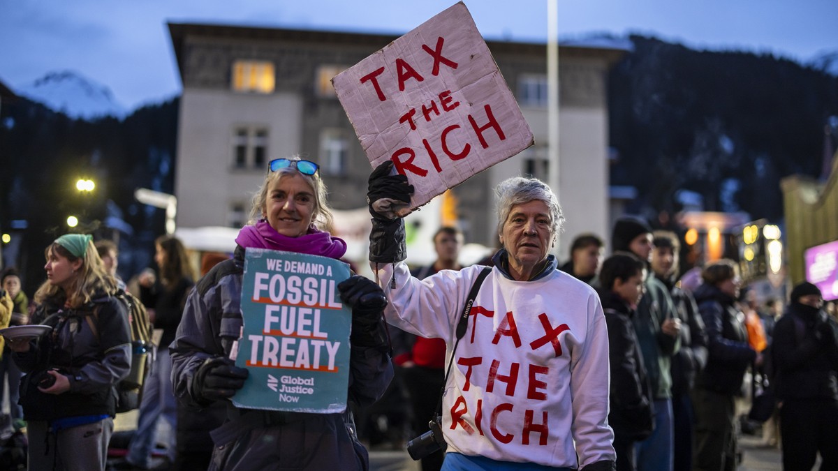 epa11836989 Phil White of Patriotic Millionaires (R) holds a placard reading "Tax the rich" as he attend a demonstration before the annual meeting of the World Economic Forum (WEF) in Davos, ...
