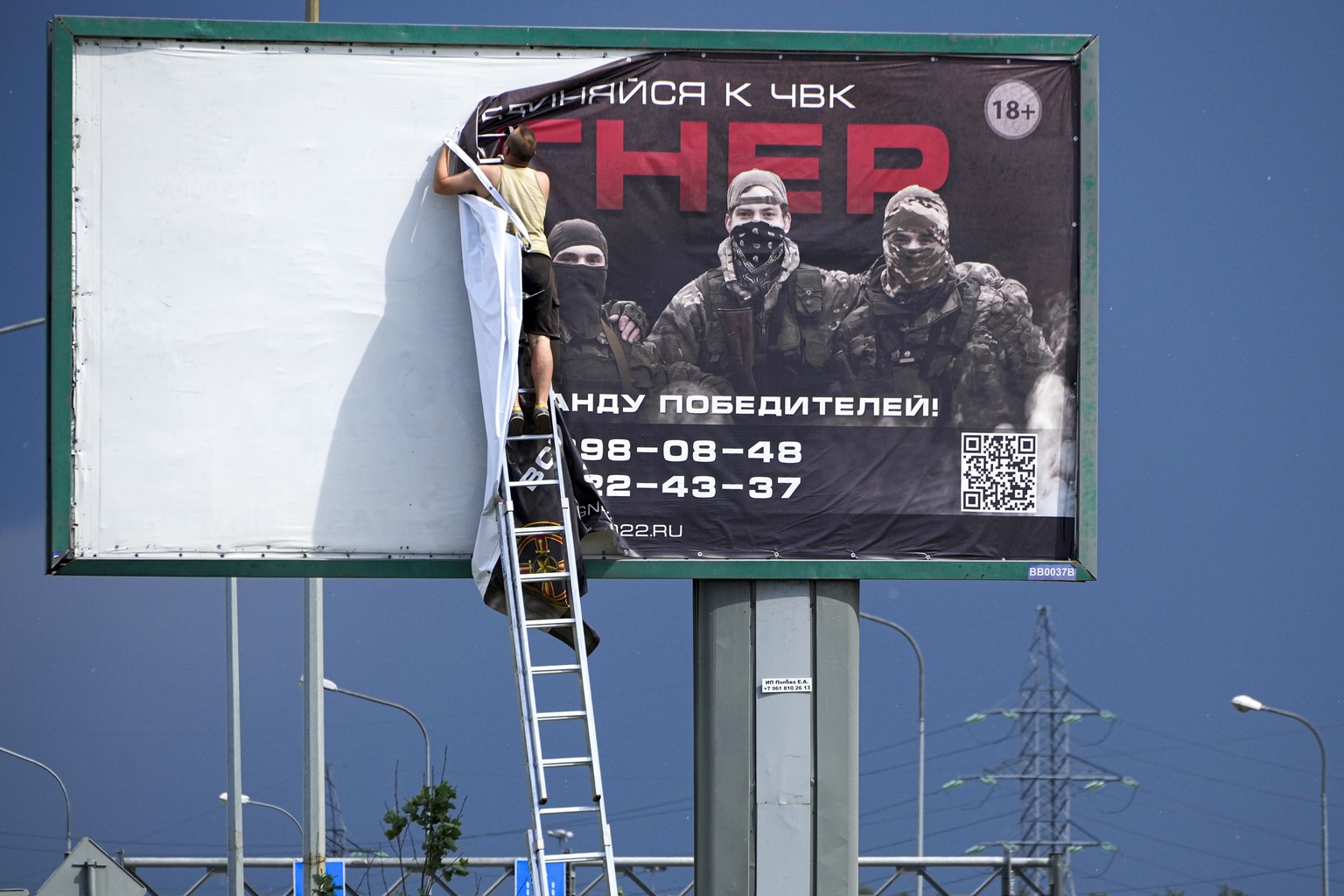 A man takes the poster with writing read "Join Wagner"which is associated with the owner of the Wagner private military contractor, Yevgeny Prigozhin, is seen over a highway...