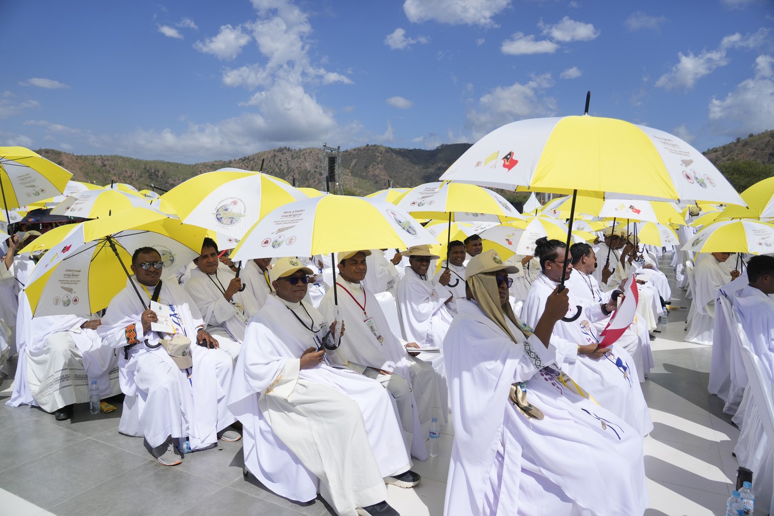 Faithful and priests use umbrellas with the colors of the Vatican flag to shield themselves from the sun as they wait for a mass presided over by Pope Francis to start in Tasitolu, some 8 kilometers w ...