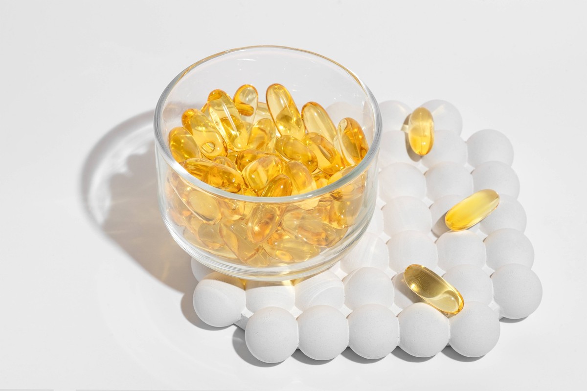 Transparent bowl filled with golden omega-3 capsules with scattered white pills around on white backdrop Ideal for health supplement promotions Model Released IrinaChetverikova_ID22098_646778_020 Copy ...