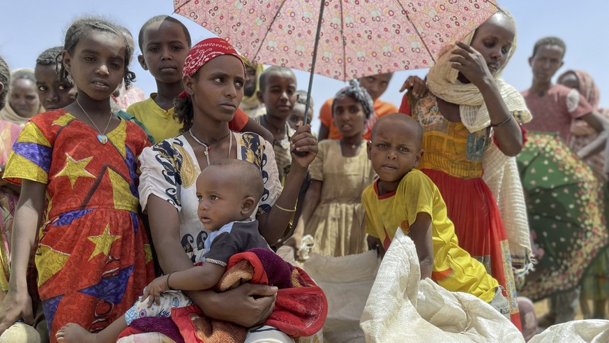 Women and children wait under the shade of an umbrella at a food distribution site in the town of Adi Mehameday, in the western Tigray region of Ethiopia, Saturday, May 28, 2022. Hunger is tightening  ...