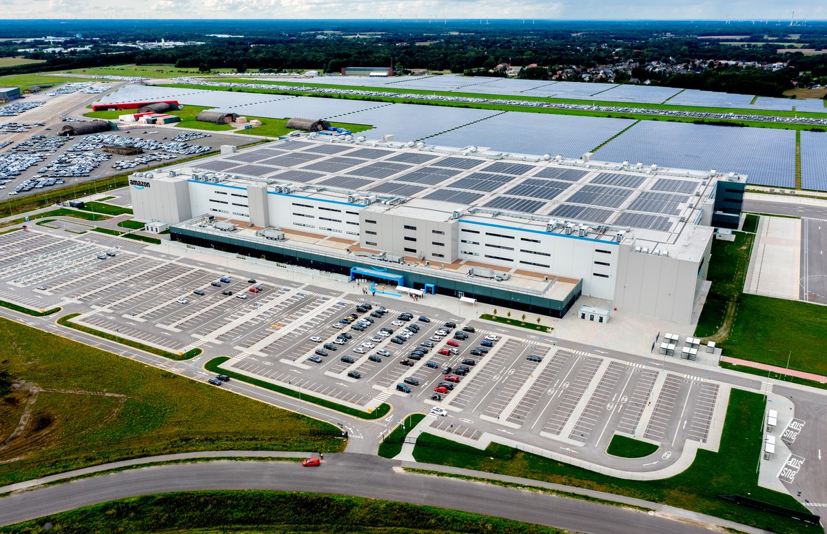 28.08.2023, Niedersachsen, Gro�enkneten: Autos stehen auf einem Parkplatz vor dem neuen Logistikzentrum von Amazon auf dem ehemaligen Fliegerhorst Ahlhorn. (Luftaufnahme mit einer Drohne) Bis Ende des ...