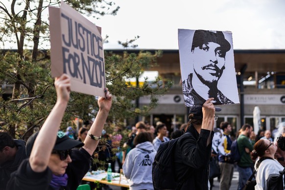 Une personne tient une banderole &quot; justice pour Nzoy &quot; et une autre personne tient le portrait de Nzoy lors d&#039;un rassemblement devant l&#039;entree de la gare CFF de Morges a la memoire ...