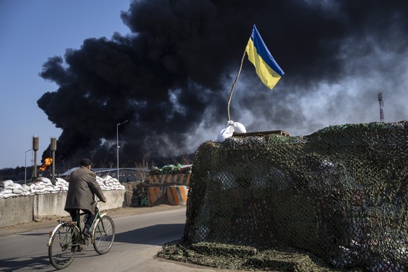 A man rides a bicycle as black smoke rises from a fuel storage of the Ukrainian army following a Russian attack, on the outskirts of Kyiv, Ukraine, Friday, March 25, 2022. (AP Photo/ (AP Photo/Rodrigo ...