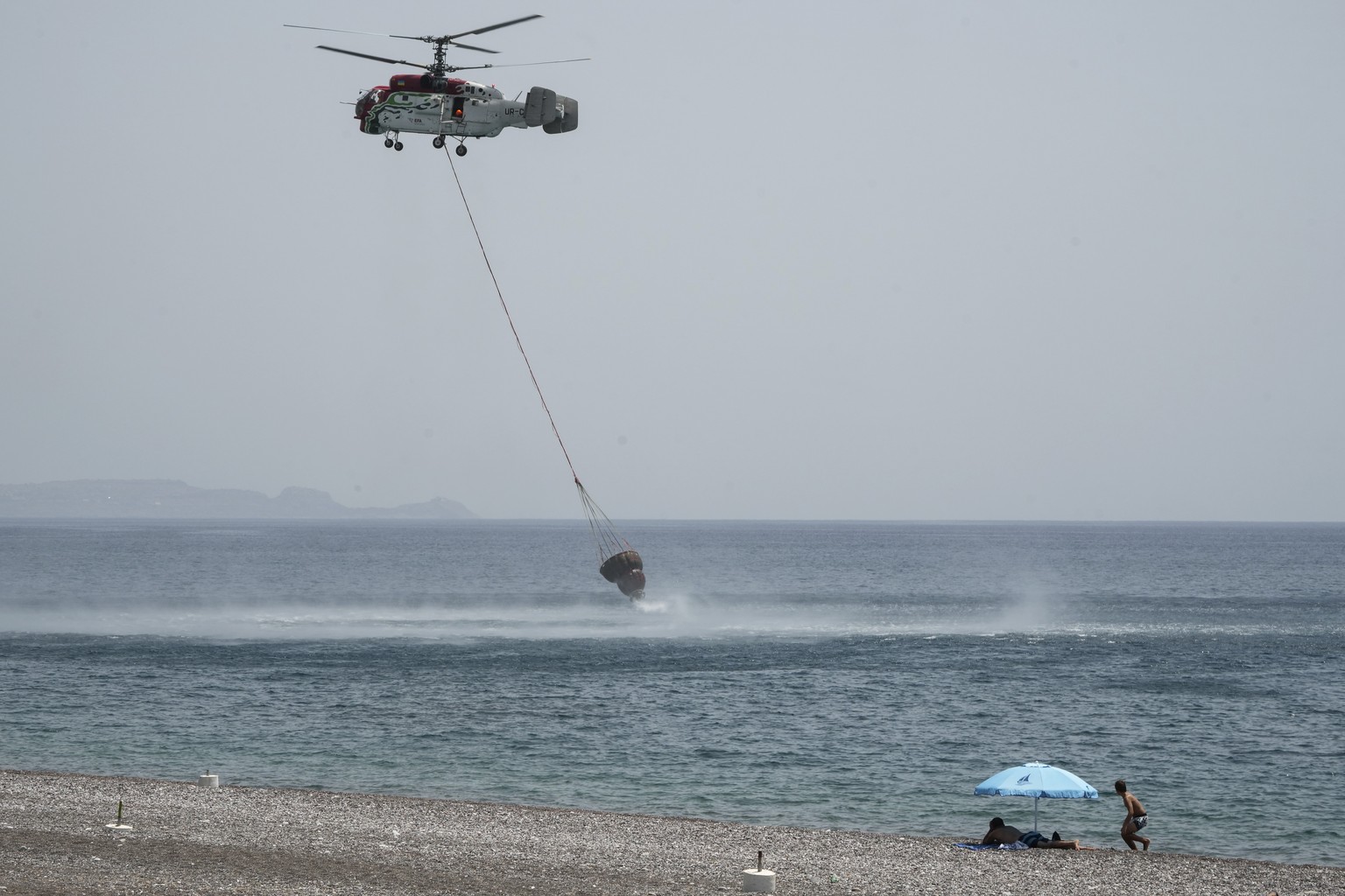 FILE - Beachgoers watch a helicopter filling water from the sea during a wildfire, near Gennadi village, on the Aegean Sea island of Rhodes, southeastern Greece, on July 27, 2023. Tourists at a seasid ...