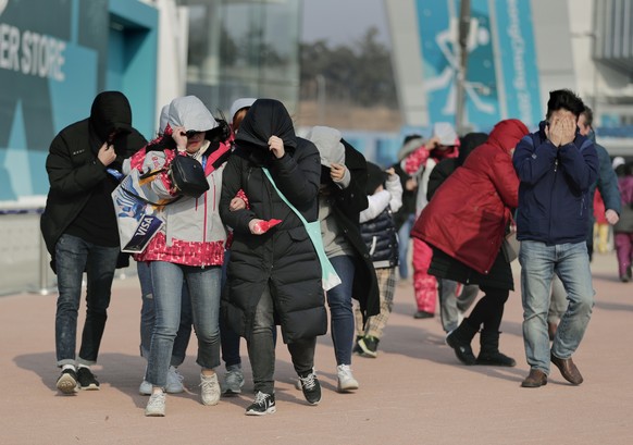 Visitors to Gangneung Olympic Park shield themselves from blowing dirt and debris from strong winds as they leave the park at the 2018 Winter Olympics in Gangneung, South Korea, Wednesday, Feb. 14, 20 ...