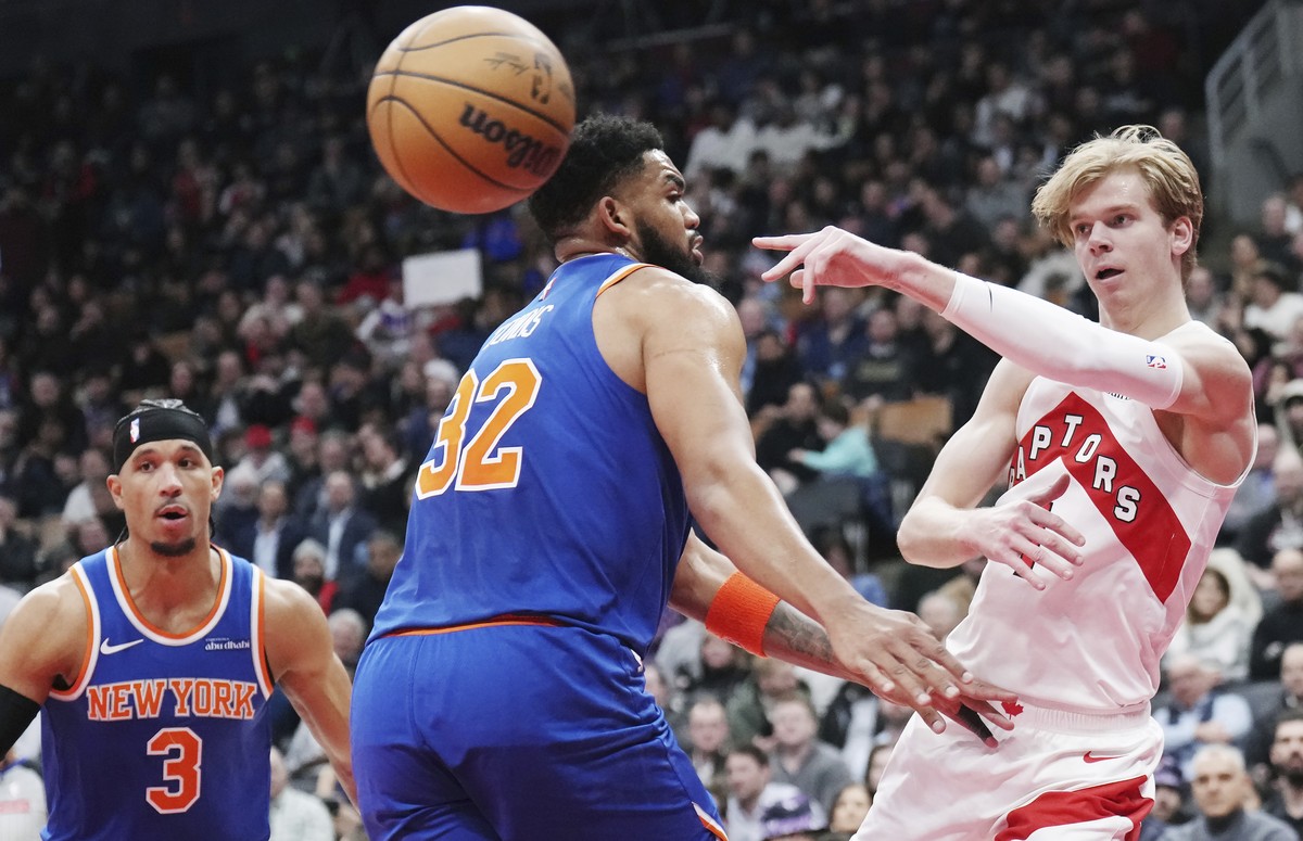 Toronto Raptors' Gradey Dick, right, passes the ball around New York Knicks' Karl-Anthony Towns (32) during the first half of an NBA basketball game in Toronto, Tuesday, Feb. 4, 2025. (Natha ...