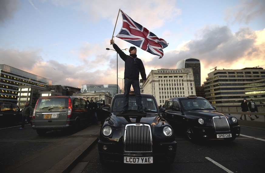 A black cab driver waves a Union flag whilst standing on a taxi a black cab drivers take part in a protest against Transport for London and Uber, on London Bridge, in the City of London, Thursday Jan. ...