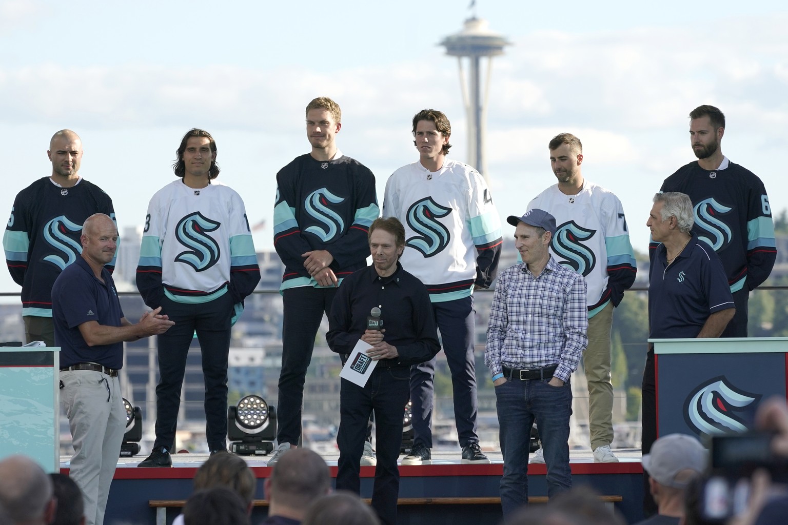 New Seattle Kraken NHL hockey players, back row from left, Mark Giordano, Brandon Tanev, Jamie Oleksiak, Hadyn Fluery, Jordan Eberle and Chris Dreidger stand on stage with Kraken owners David Wright,  ...