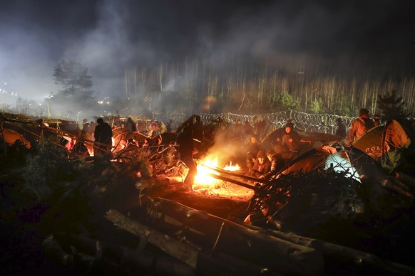 Migrants warm themselves at a fire in frigid conditions as they gather at the Belarus-Poland border near Grodno, Belarus, Saturday, Nov. 13, 2021. Belarusian state news agency Belta reported that Luka ...