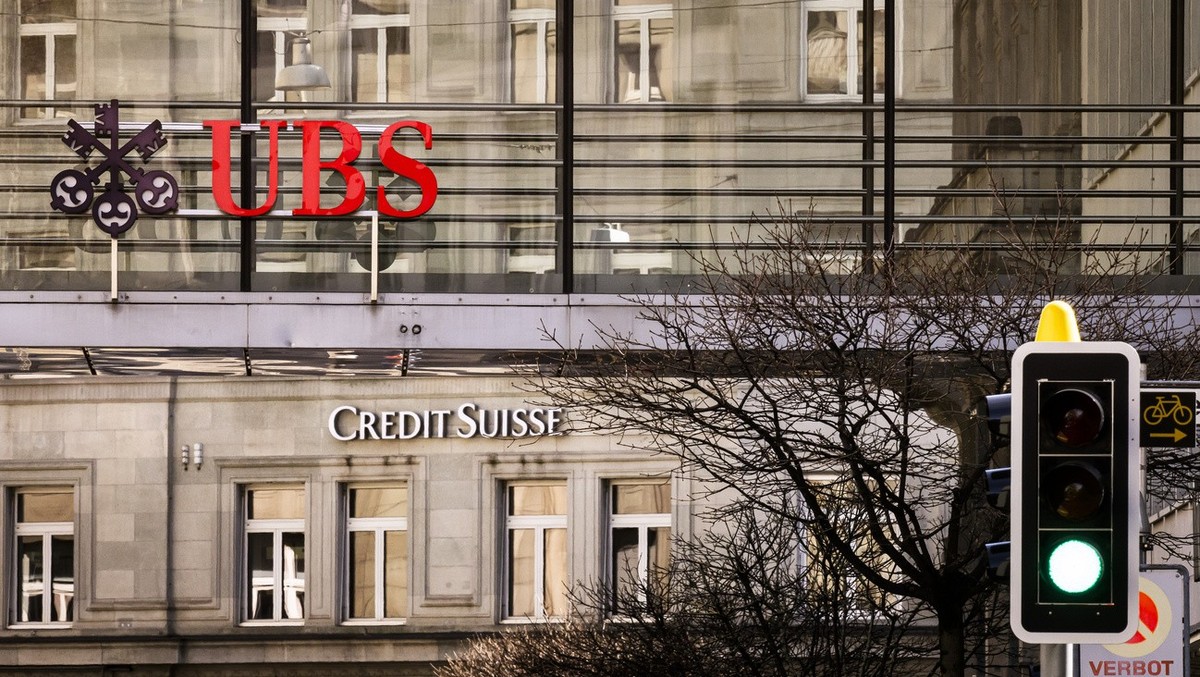 Logos of the Swiss banks Credit Suisse and UBS are seen next to traffic lights on two buildings in Zurich, Switzerland on Saturday, March 18, 2023. (KEYSTONE/Michael Buholzer).