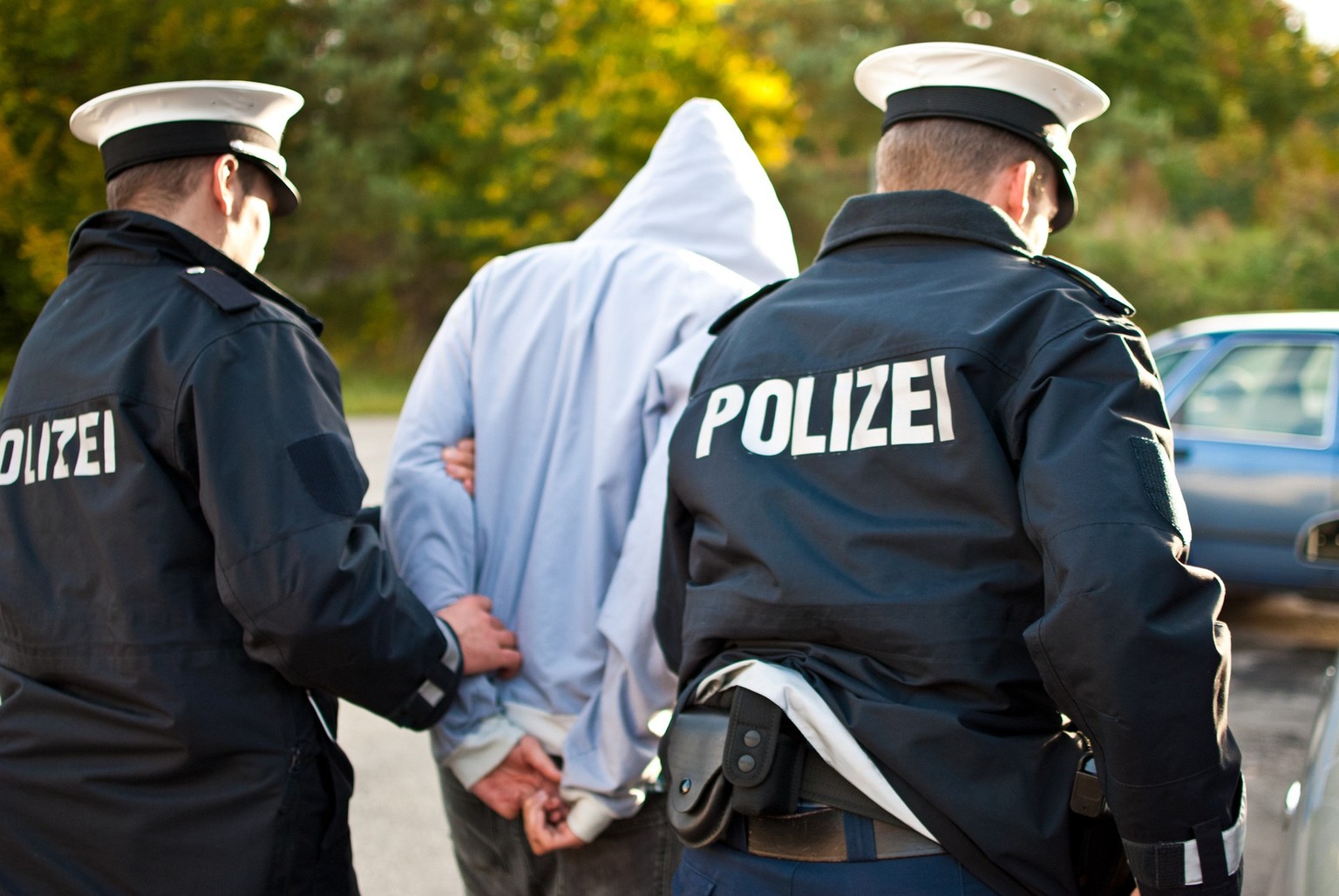 Two police officers are frogmarching a criminal with a mask.