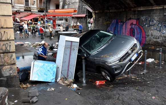 epa11668252 A man walks past a car that was carried away by flooding water in central area of Catania, Italy, 19 October 2024. Torrential rain in Catania and its province caused flooding and damage. D ...
