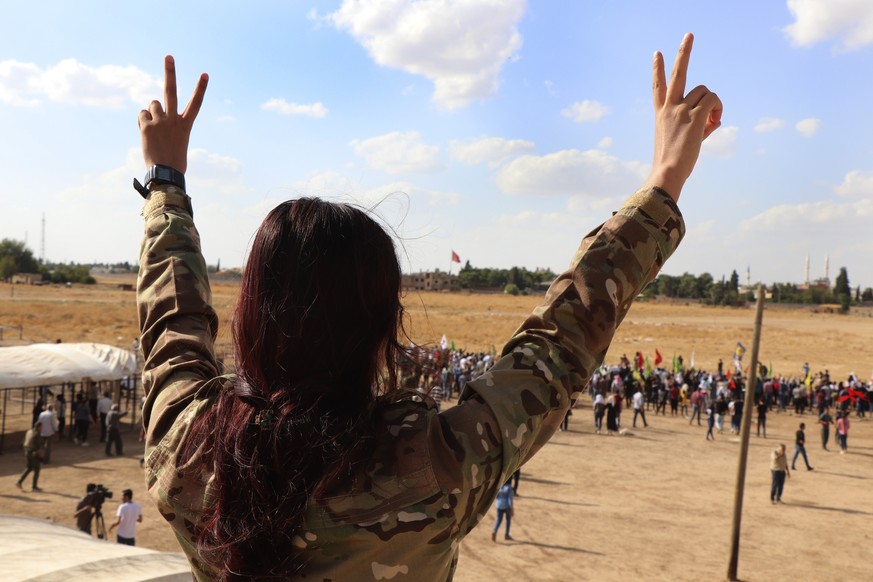 A fighter from the Syrian Democratic Forces, SDF, flashes the victory sign during a demonstration against possible Turkish military operation on their areas, at the Syrian-Turkish border, in Ras al-Ay ...