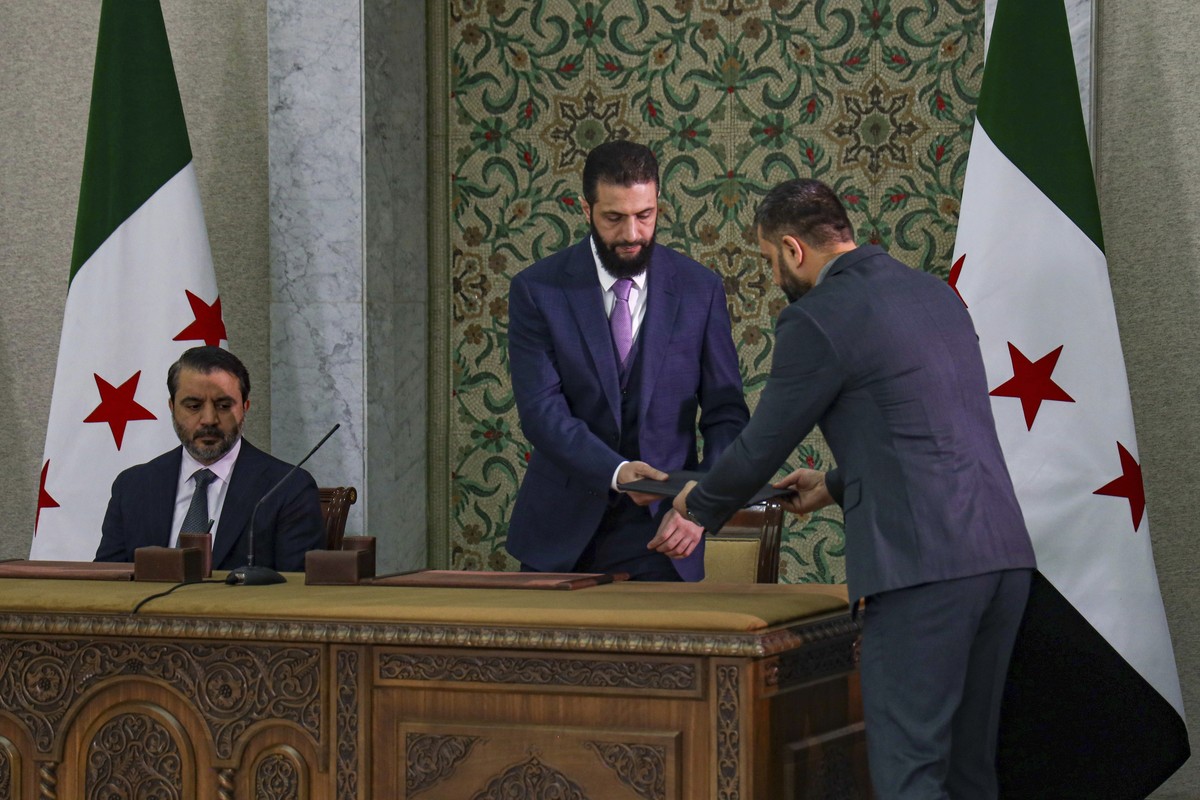 Syria's interim president Ahmad Al-Sharaa, center, prepares to sign a temporary constitution for the country in Damascus, Syria, Thursday March 13, 2025. At left, is Foreign Minister Asaad Hassan ...