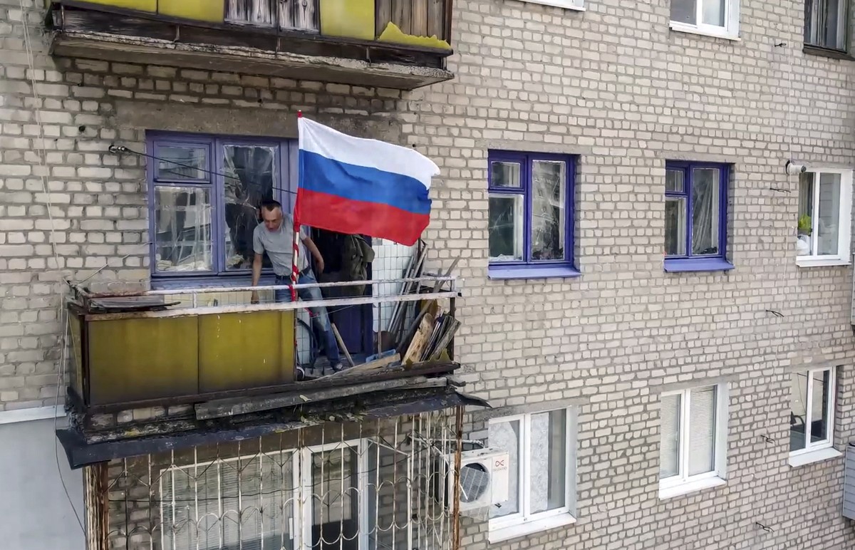 epa10051474 A still image taken from a handout video provided by the Russian Defence Ministry press service shows a local man flying the Russian flag on his balcony in Lysychansk, Luhansk region, Ukra ...