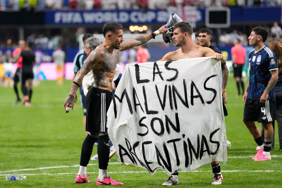 Argentina's Giovani Lo Celso holds a banner with the words "The Malvinas are Argentine", referring to the Falkland Islands, while teammate Argentina's Nicolas Otamendi gestures to  ...