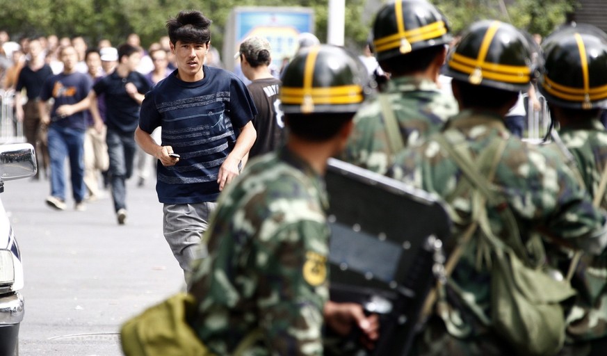 epa01787319 A men belonging to the Chinese Uyghur Moslem miniority (C) runs from Han Chinese armed with clubs and metal pipes towards a line of soldiers to get access to a Uyghur neighbourhood in Urum ...