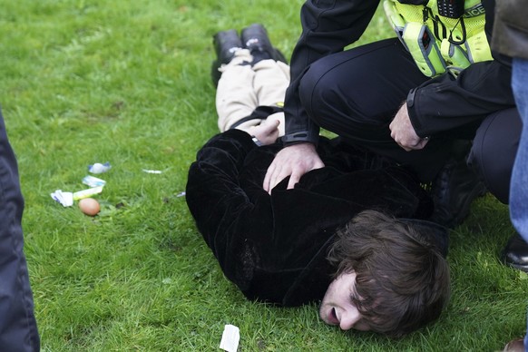 Police empty contents, including an unthrown egg, left, from the pockets of a protester, as they detain him for throwing eggs at Britain&#039;s King Charles III and Camilla, the Queen Consort, as they ...