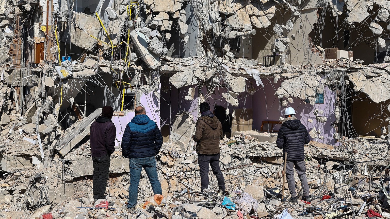 epa10467880 People stand at a site of collapsed buildings after a powerful earthquake, in Hatay, Turkey, 15 February 2023. More than 41,000 people died and thousands more were injured after two major  ...
