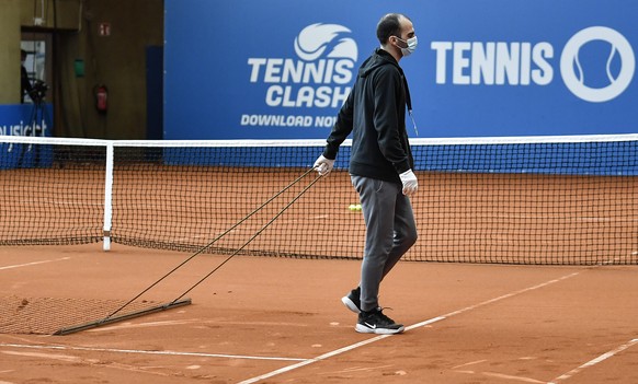 A helper with a face mask prepares the court at a pro-tennis tournament at a local base tennis academy in Hoehr-Grenzhausen, western Germany, Friday, May 1, 2020. The professional tennis exhibition in ...