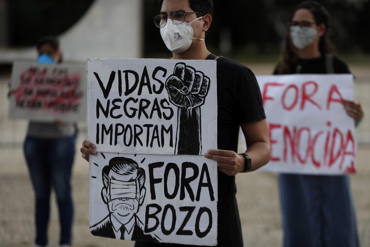 An activist holds signs that read in Portuguese "Black Lives Matter," and "Bolsonaro Out," during a demonstration marking the day slavery was abolished in Brazil, and against gover ...