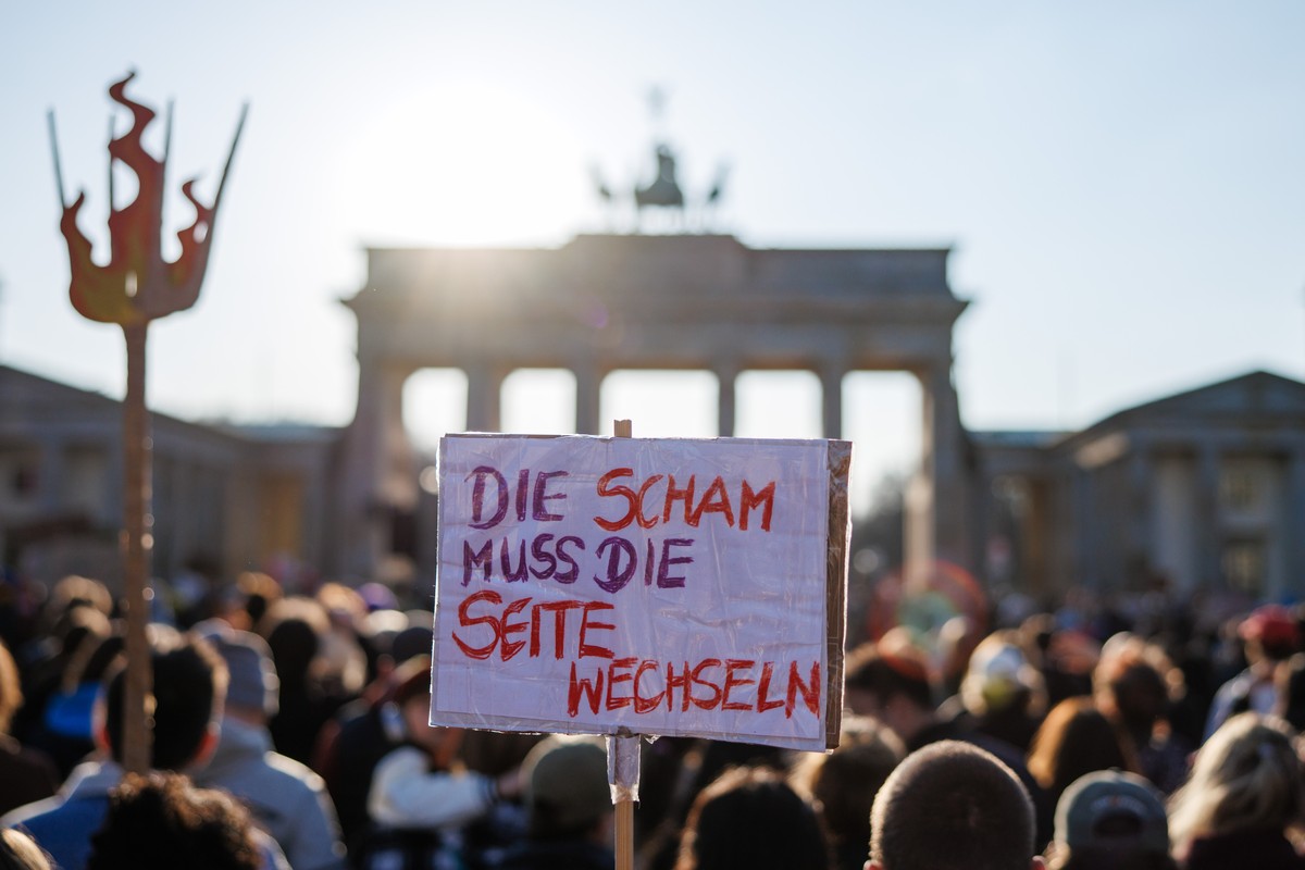 epa12841836 A participant holds a placard that reads 'Shame has to change sides' during a rally at the Brandenburg Gate in Berlin, Germany, 22 March 2026. The rally took place under the mott ...