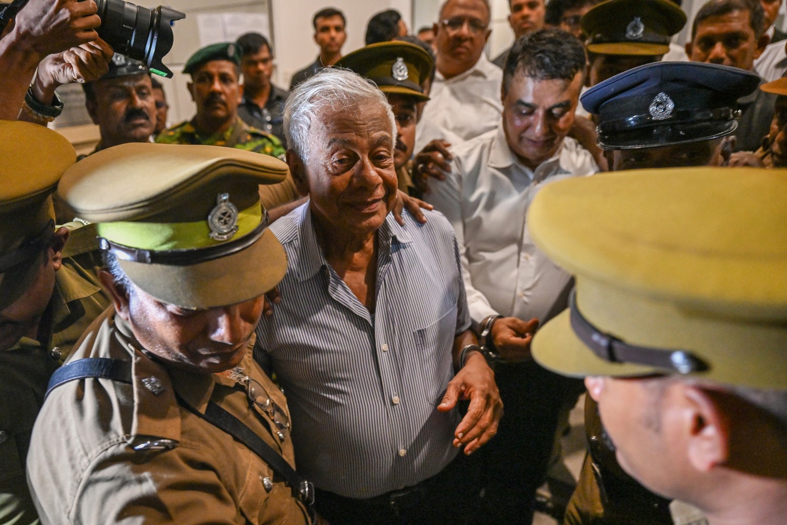 Sri Lankan police officials escort former Defense Ministry Secretary Hemasiri Fernando, center left, and former Police Chief Pujith Jayasundara, center right, outside a court in Colombo, Sri Lanka, Fr ...