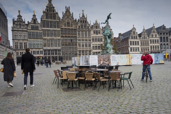 People walk by chairs and tables of an empty terrace in the historical center of Antwerp, Belgium, Sunday, Oct. 18, 2020. Faced with a resurgence of coronavirus cases, the Belgian government on Friday announced new restrictions to try to hold the disease in check, including a night-time curfew and the closure of cafes, bars and restaurants for a month. The measures will take effect on Monday, Oct. 19, 2020. (AP Photo/Virginia Mayo)