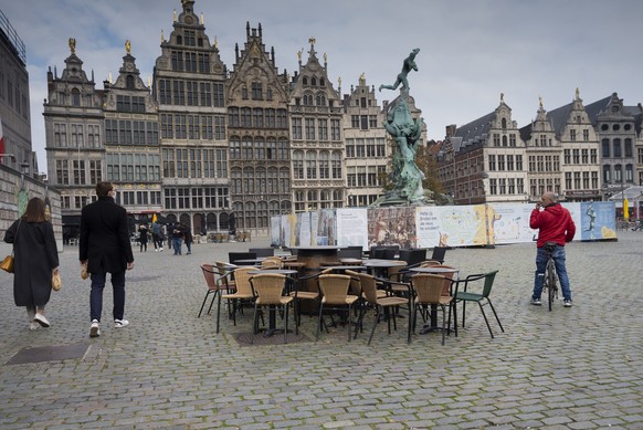 People walk by chairs and tables of an empty terrace in the historical center of Antwerp, Belgium, Sunday, Oct. 18, 2020. Faced with a resurgence of coronavirus cases, the Belgian government on Friday ...