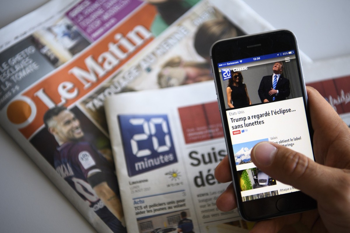 Une personne observe l' app de 20 Minutes sur son iPhone devant le journal Le Matin et photographie a cote du journal 20 Minutes ce mardi 22 aout 2017 a Lausanne. Les redactions des quotidiens 20 ...