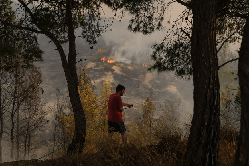 A man tries to extinguish the fire with a hose near Loutraki 80 Kilometres west of Athens, Monday, July 17, 2023. Greater Athens and much of southern Greece were on the second highest alert for wildfi ...