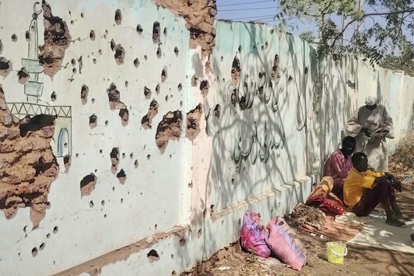 In this video frame, displaced Sudanese sit next to a bullet-riddled wall, taking shelter in a school after being evacuated by the Sudanese army from areas once controlled by the paramilitary Rapid Su ...
