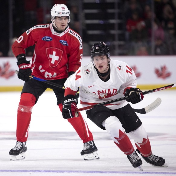 Switzerland's Lian Bichsel, left, and Canada's Zach Dean watch as the puck clears the Canadian zone during first-period IIHF World Junior Hockey Championship pretournament hockey game action ...